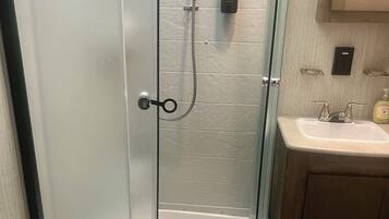 A bathroom with a glass-enclosed shower, a toilet, a sink, and toiletries on the wall.