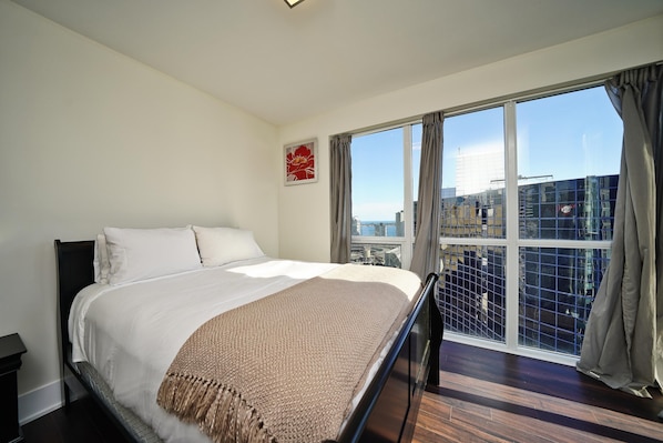 A hotel room with a large bed, a view of the city through floor-to-ceiling windows, and a cityscape visible outside. - Northcrest Hotel (Toronto)