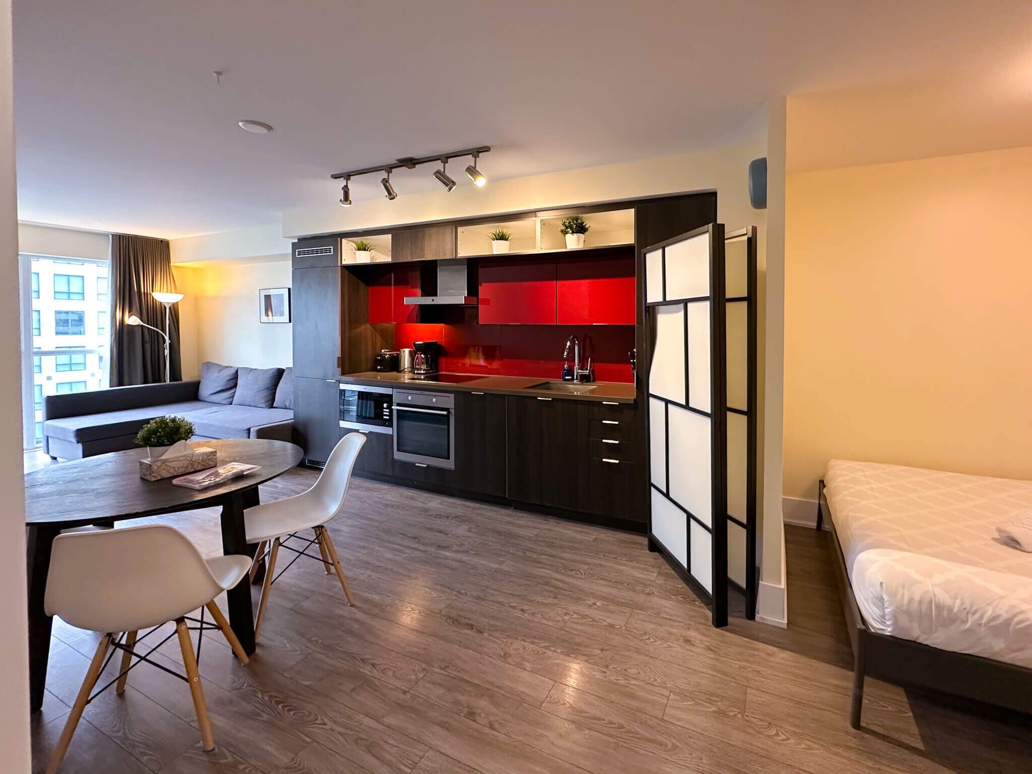 A compact living space with a kitchenette, a dining area with a table and chairs, a sofa, and a bed.