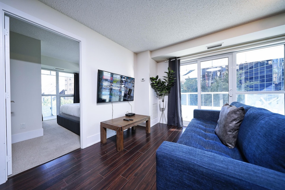 A living room with a blue sofa, a wooden coffee table, a flat-screen TV, and a large window with a view of buildings.