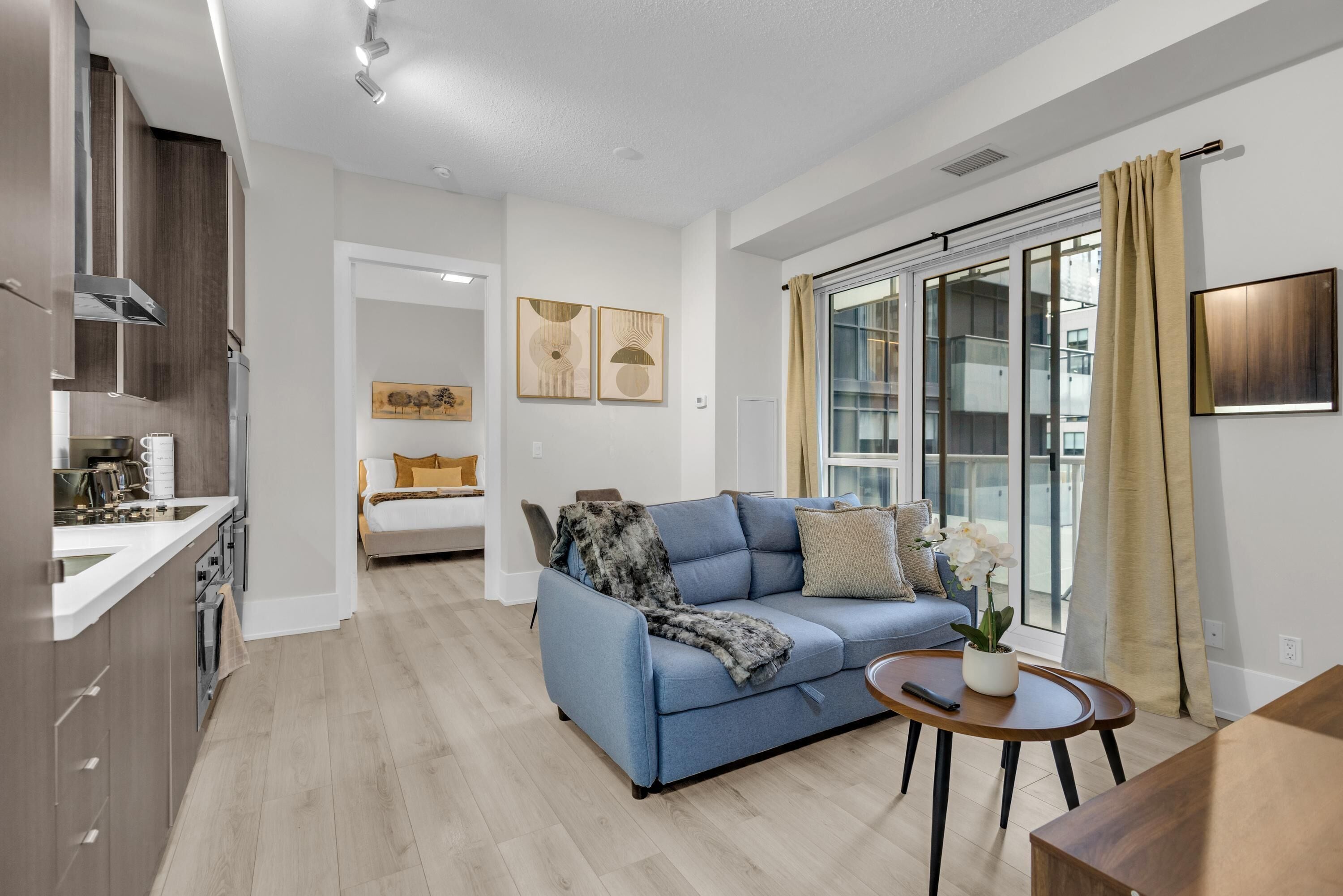 A modern apartment with a kitchen, a living area with a sofa and coffee table, and a large sliding glass door to the balcony.