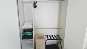 A closet with a hanging rack, shelves with folded clothes, and a storage box.