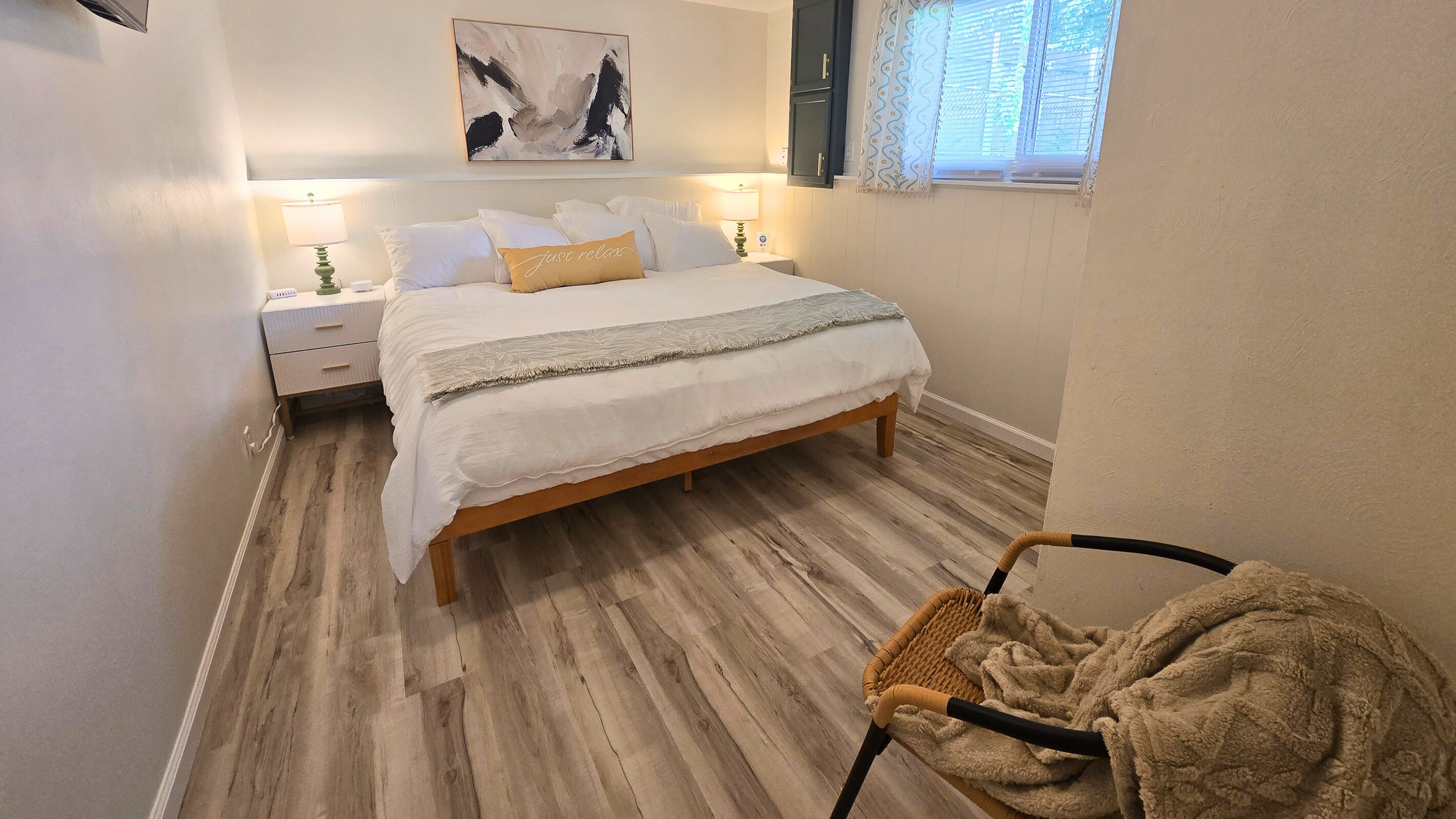 Een slaapkamer met een bed, nachtkastjes, een stoel, een raam en een schilderij aan de muur.