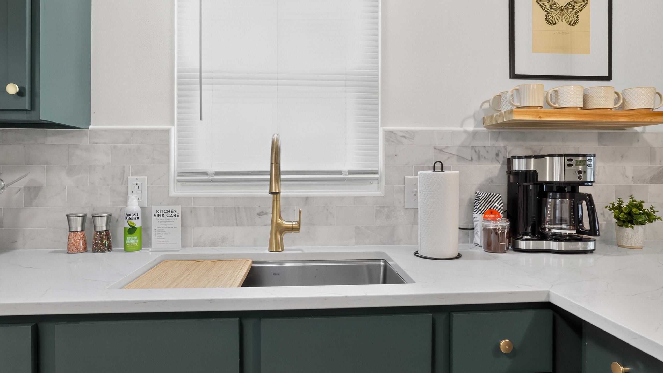 A kitchen with a modern faucet, a coffee maker, and a window with blinds.