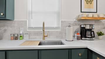A kitchen with a modern faucet, a coffee maker, and a window with blinds.