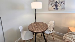 A small round table with two chairs, a floor lamp, and a wall art piece.