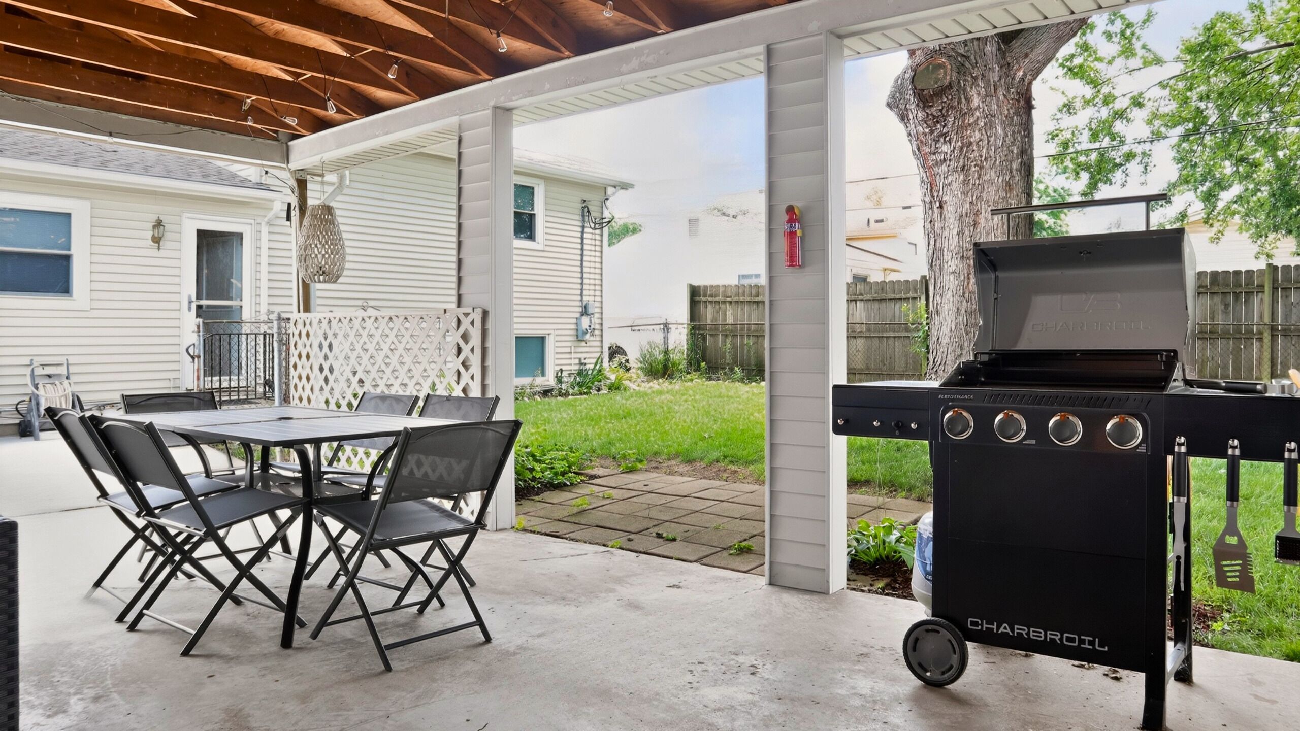 An outdoor patio with a grill, a table with chairs, and a covered area.