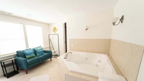 Un baño con bañera, ventana, sofá y una mesita.