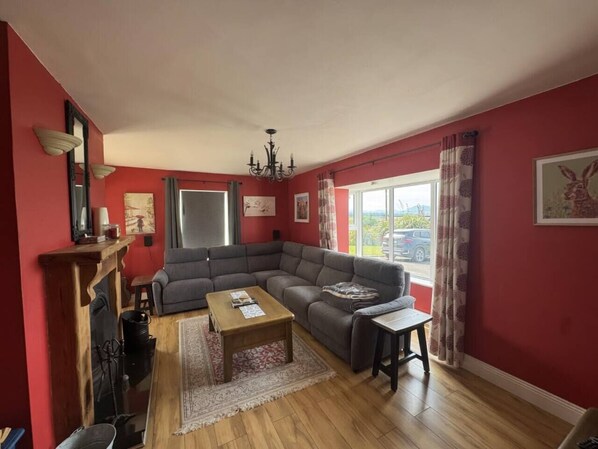A living room with a sectional sofa, a wooden coffee table, a fireplace, and a large window with curtains.