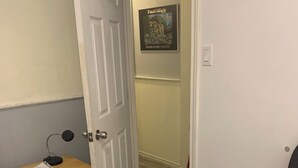Een kamer met een bed, een klein tafeltje met een lamp, een stoel en een deur naar een andere kamer.