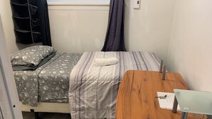 Een eenvoudige kamer met een bed, een houten tafel en een raam met gordijnen.