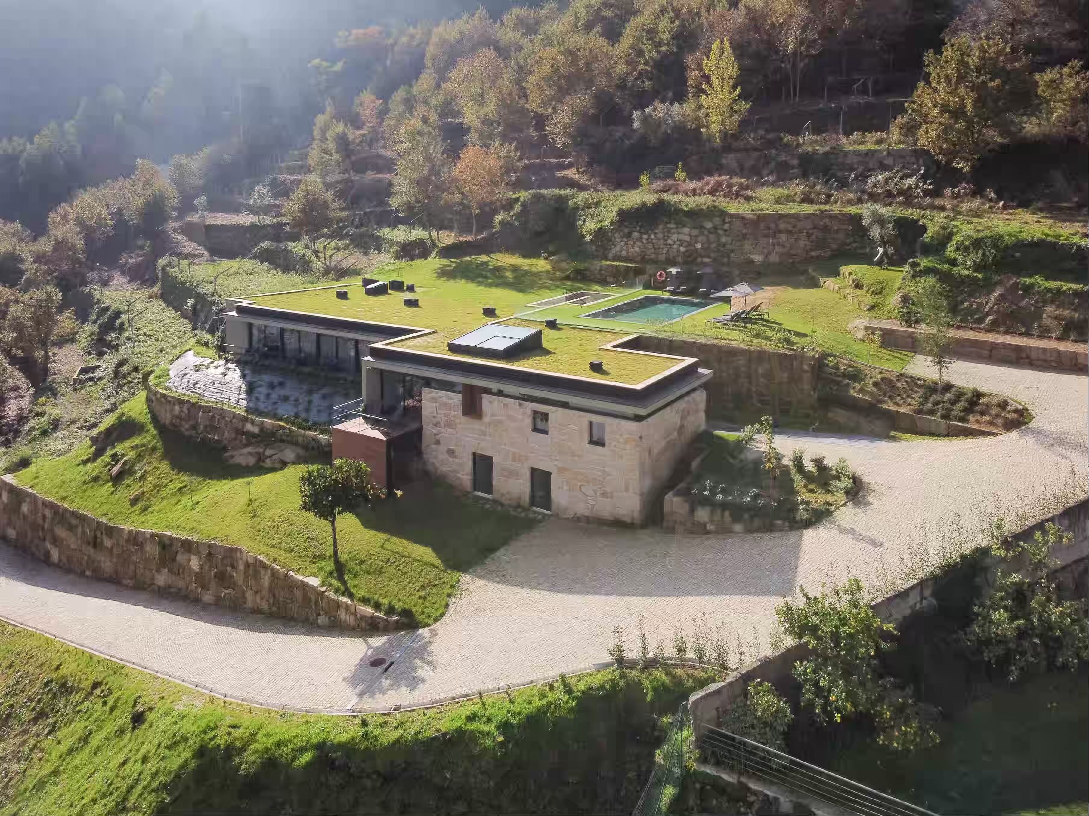 A modern building with a flat roof, surrounded by terraced gardens and a stone wall.