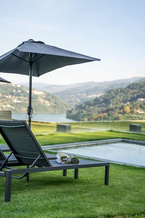 Zona relax amb gandules al costat d'una piscina, amb vista a un llac i a les colines.