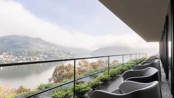 A balcony with a view of a river and a town, featuring modern chairs and a metal railing.