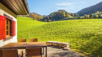 A patio with a table and chairs, overlooking a lush green field and a hillside.