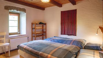 A bedroom with a wooden bed, a bench, a window, a radiator, and a hanging light fixture.