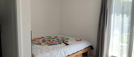 Une chambre à coucher avec un lit, un banc en bois, une fenêtre avec des rideaux et un tapis rouge.