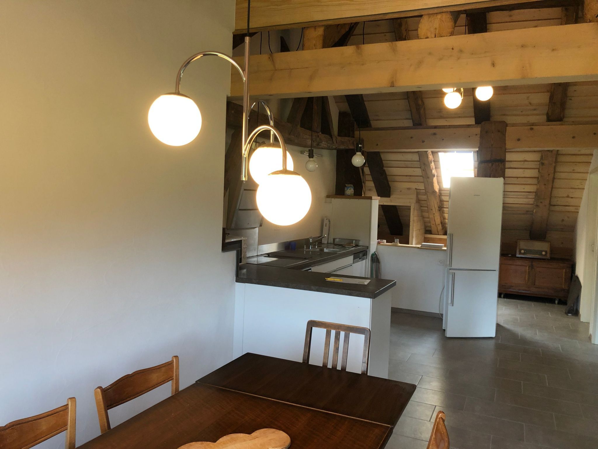 Cozinha com mesa e cadeiras, vigas de madeira no teto e uma geladeira.