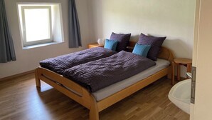Ein Schlafzimmer mit einem Holzbett, einem Nachttisch, einem Fenster mit Vorhängen und Holzboden.