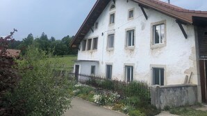 Ein zweistöckiges Gebäude mit geneigtem Dach, zahlreichen Fenstern und einem kleinen Gartenbereich mit einem Metallzaun.