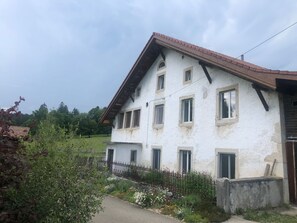 A two-story building with a sloped roof and multiple windows. - Appartement et B&B - Ferme O'Badu, (Les Breuleux), by Interhome (Les Breuleux)