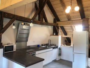 A kitchen with a built-in microwave, stove, and refrigerator, featuring exposed wooden beams and pendant lighting. - Appartement et B&B - Ferme O'Badu, (Les Breuleux), by Interhome (Les Breuleux)
