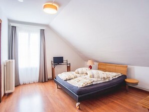 Ein Schlafzimmer mit einem Bett, einem Nachttisch, einer Lampe, einem Heizkörper und einem Fenster mit Vorhängen.