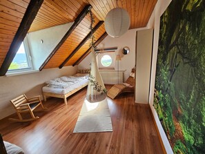 A cozy attic bedroom with a sloped ceiling, a bed, a rocking chair, and a large window. - Appartement - Le Solvat, (Courcelon), by Interhome (Courcelon)