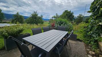 An outdoor patio with a wooden table and chairs, surrounded by greenery and a scenic view.