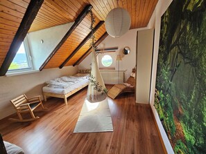 Ein Schlafzimmer mit schrägen Wänden, einem Bett, einem Schaukelstuhl, einem Hängesessel und einem großen Fenster.