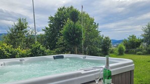 Boblebad med en flaske RIMAS vin og to glas på et bord, omgivet af grøn vegetation og udsigt over landskabet.