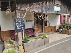 A rustic building with a wooden exterior, a chalkboard sign listing local products, and a small garden area with planters. - Appartement - Le Solvat, (Courcelon), by Interhome (Courcelon)