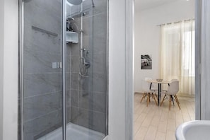 A modern bathroom with a glass-enclosed shower, a white bathtub, and a dining area with a table and chairs. - Myla's rooms (Palermo)