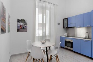 A modern kitchen with blue cabinets, a white dining table with chairs, and a large window with sheer curtains. - Myla's rooms (Palermo)