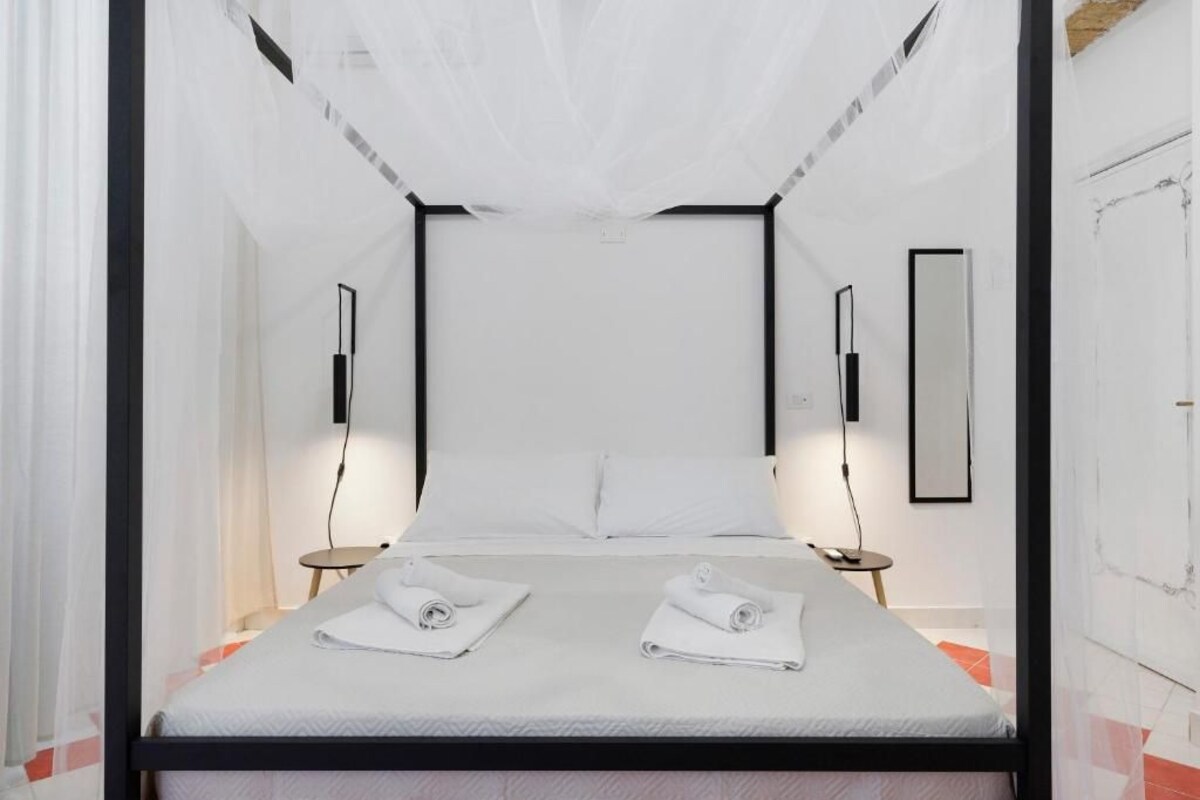 A hotel room with a bed, two bedside tables, and a large window with curtains.