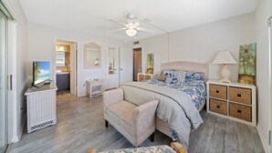 A bedroom with a bed, a chair, a TV, a ceiling fan, a nightstand, and a dresser. - Stay Where The Rockets Launch & The Waves Roll In! (Satellite Beach)
