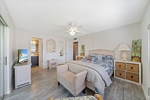 Ein Schlafzimmer mit Bett, Stuhl, Fernseher, Deckenventilator und Kommode.
