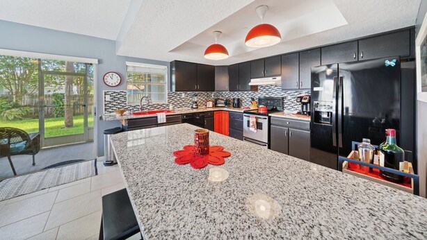 A modern kitchen with granite countertops, black cabinets, and stainless steel appliances. - Stay Where The Rockets Launch & The Waves Roll In! (Satellite Beach)