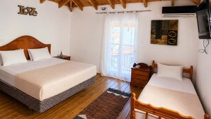 Ein Schlafzimmer mit einem großen Bett, einem kleineren Bett, Holzbalken an der Decke, einem an der Wand montierten Fernseher und einem Fenster mit Vorhängen.