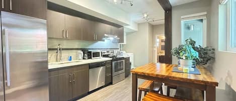 A modern kitchen with stainless steel appliances, wooden cabinets, and a wooden dining table with benches.