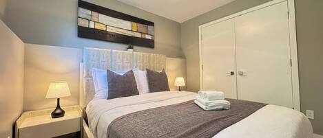 A neatly made bed with pillows, a bedside lamp, a wall art piece, and a wardrobe.