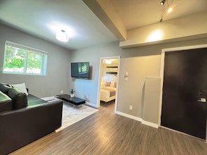 A modern living room with a flat-screen TV, a sofa, a coffee table, and a dining area.