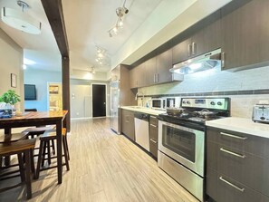 A modern kitchen with stainless steel appliances, wooden cabinets, and a dining area with a wooden table and chairs. - Garden basement suite in Edgemont Village, perfect for Capilano, Grouse Mtn., and FIFA. Quiet, safe area with a bus 5 minutes away for easy downtown access. Walk to shops, cafés, groceries, and more. (North Vancouver)