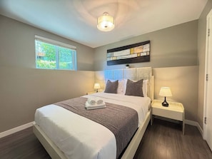 A hotel room with a large bed, two bedside lamps, a window with a view of greenery, and a ceiling light fixture.