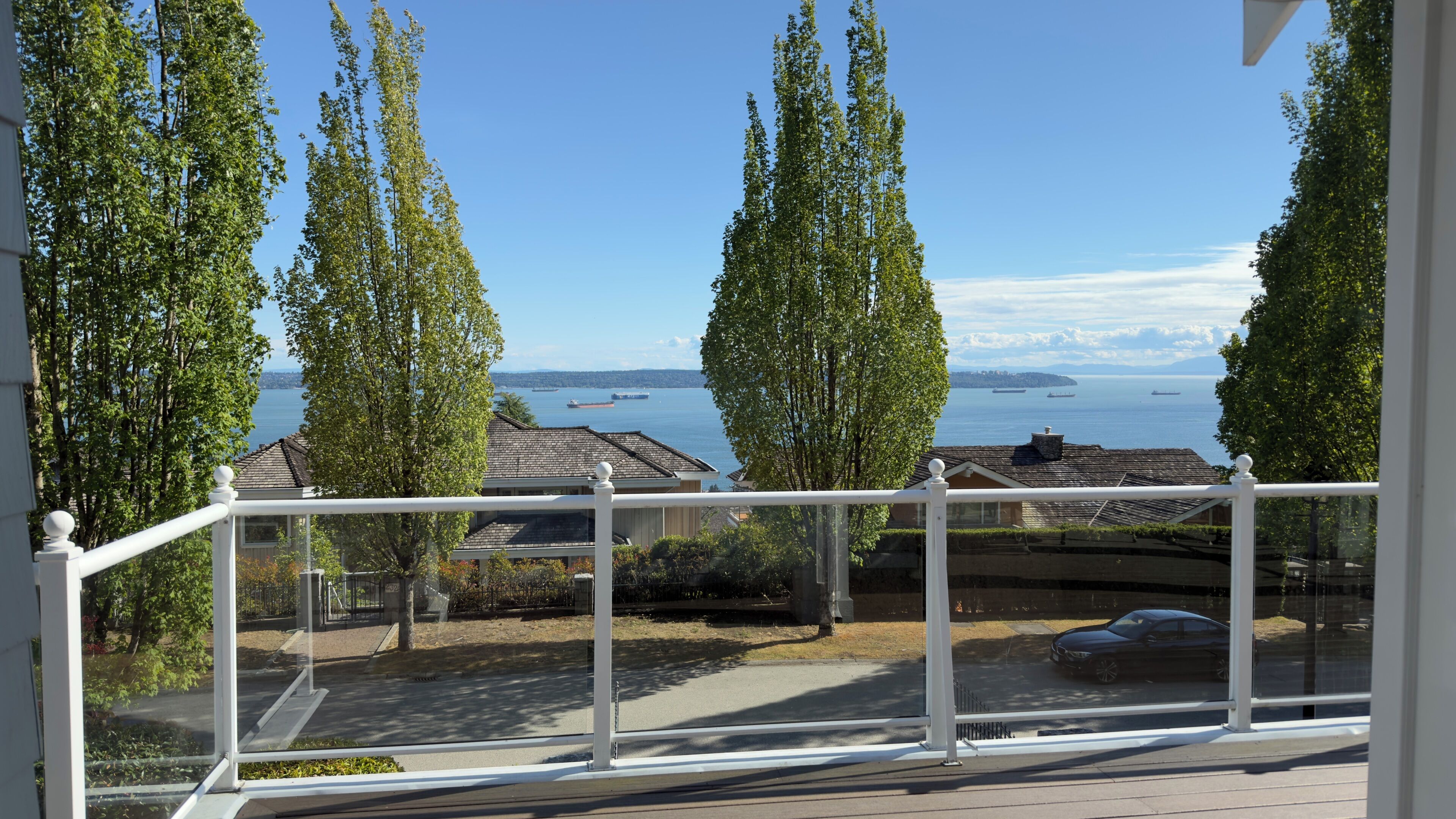 A balcony with a view of the sea and a car parked in the driveway.