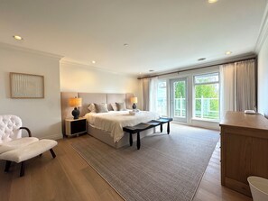 Ein Schlafzimmer mit einem Bett, Nachttischen, einem Sessel, einer Bank und Blick ins Freie durch ein großes Fenster.