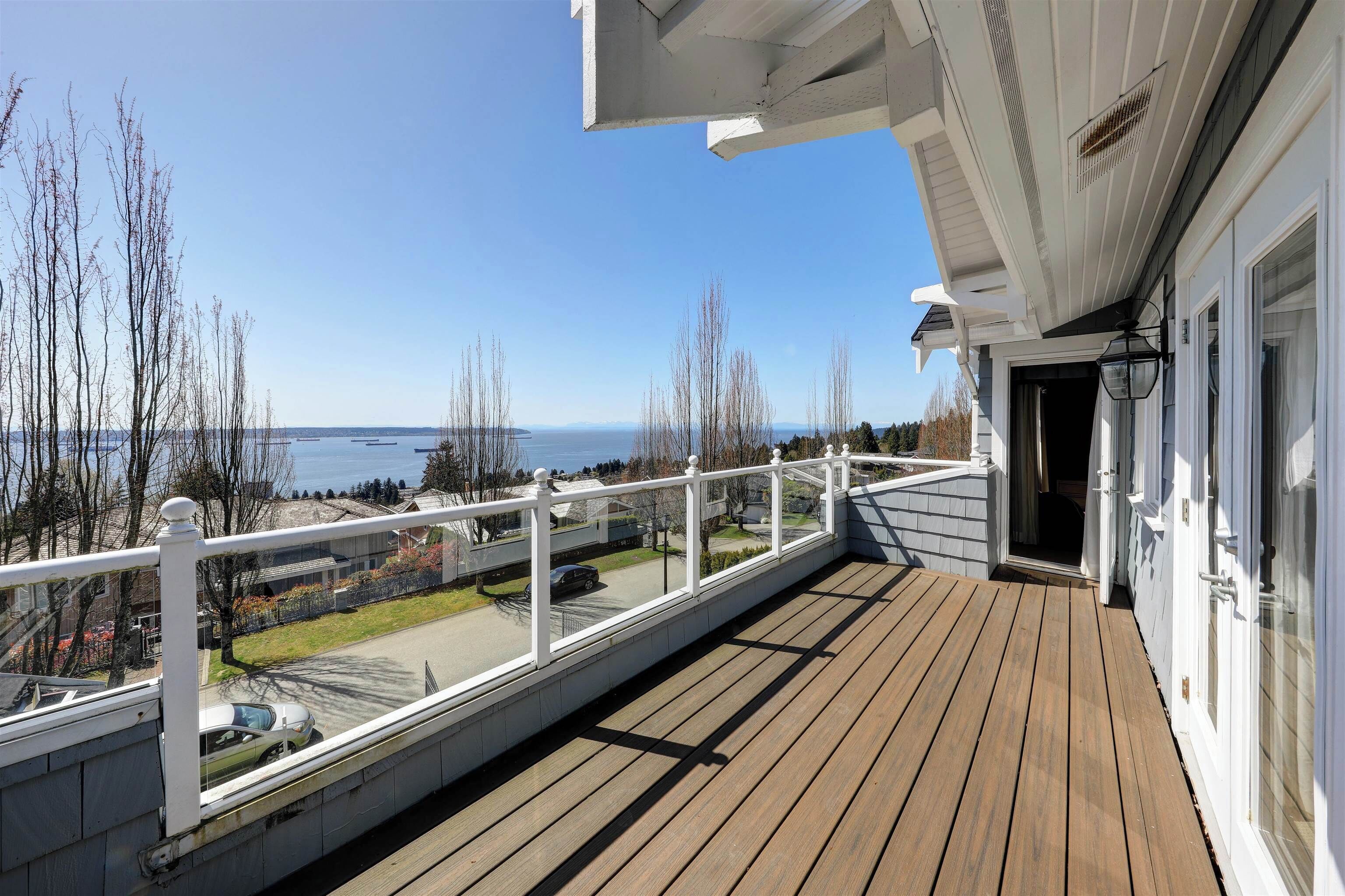 A wooden deck with a white railing, a clear view of the sea, and a building with a white facade.