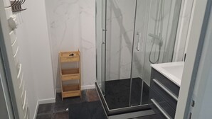 Ett badrum med en dusch som är avskärmad med glasväggar, en hylla i trä och en svart matta.