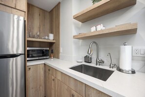 Eine moderne Küche mit Edelstahl-Kühlschrank, Mikrowelle und doppelter Spüle. Holzschränke und eine Marmorarbeitsplatte sind ebenfalls zu sehen.