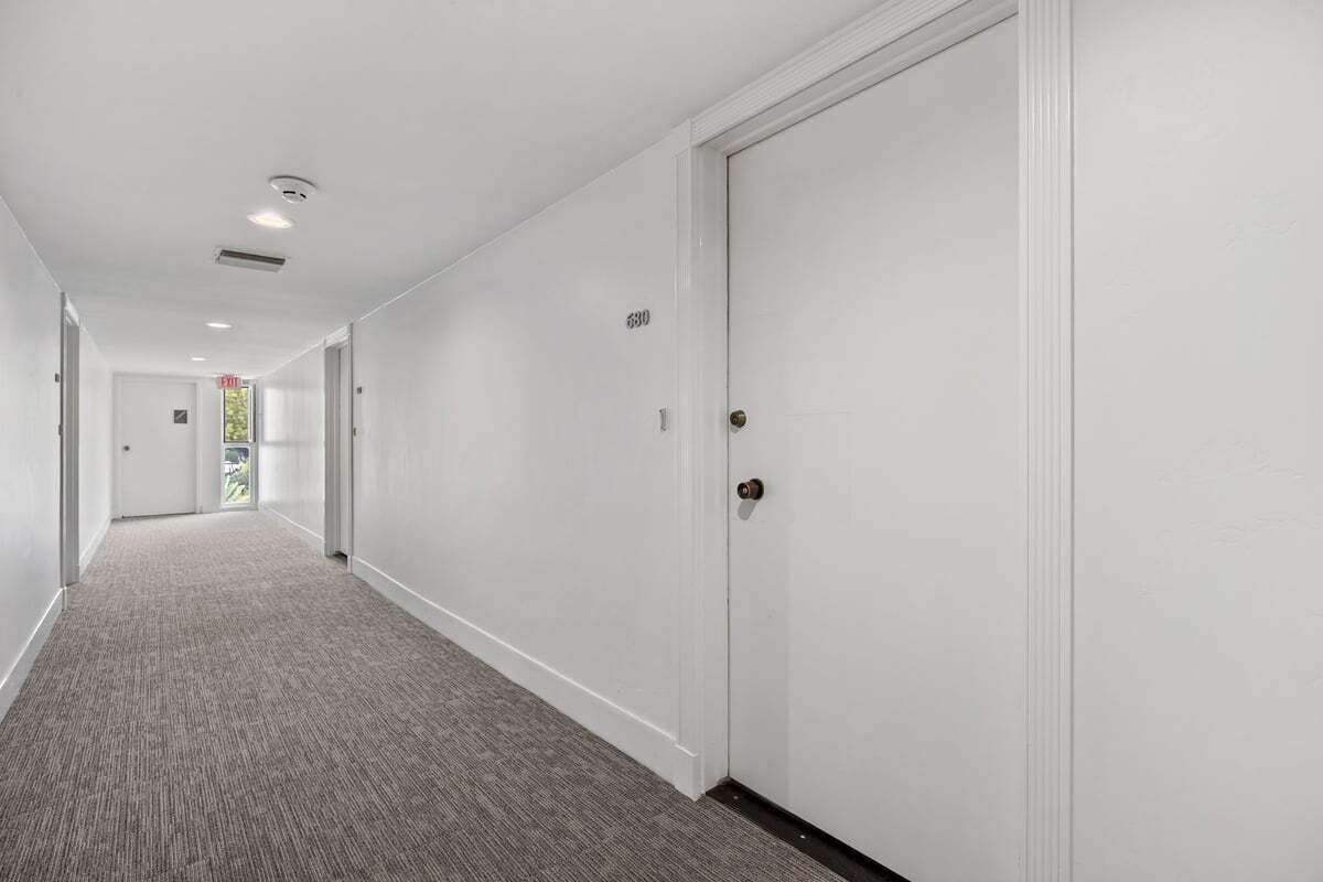 A corridor with a carpeted floor, white walls, and doors with numbers.